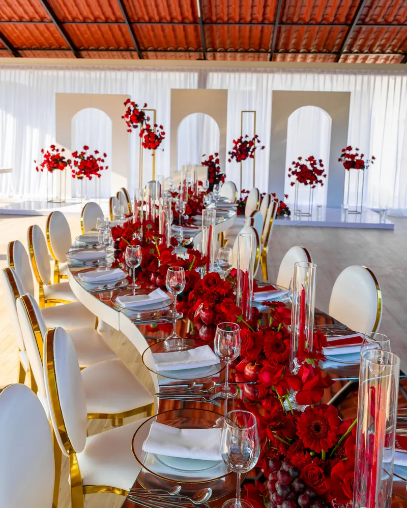 Mesa larga con rosas rojas, velas y sillas doradas