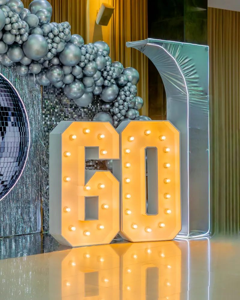 Letras iluminadas de 60 junto a la guirnalda de globos plateados