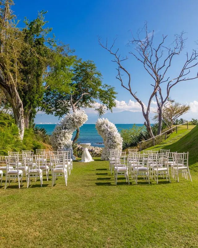 Ceremonia en jardín frente al mar con arcos de flor blanca
