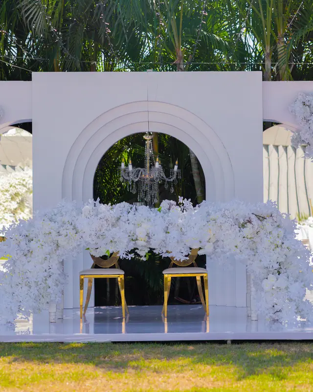 Arco blanco con flor y mesa de novios sobre tarima