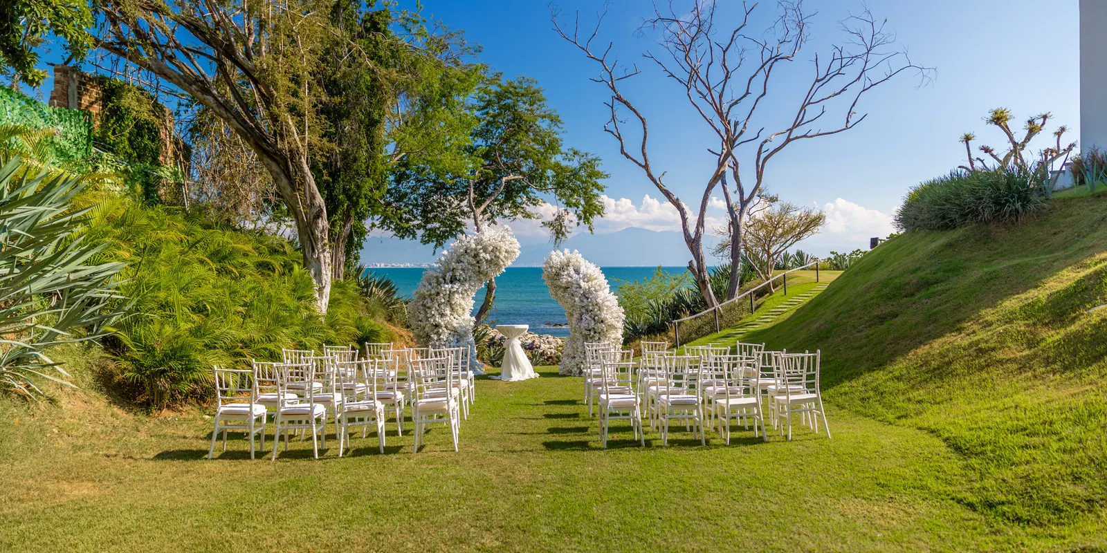 Ceremonia en jardín frente al mar con arcos de flor blanca